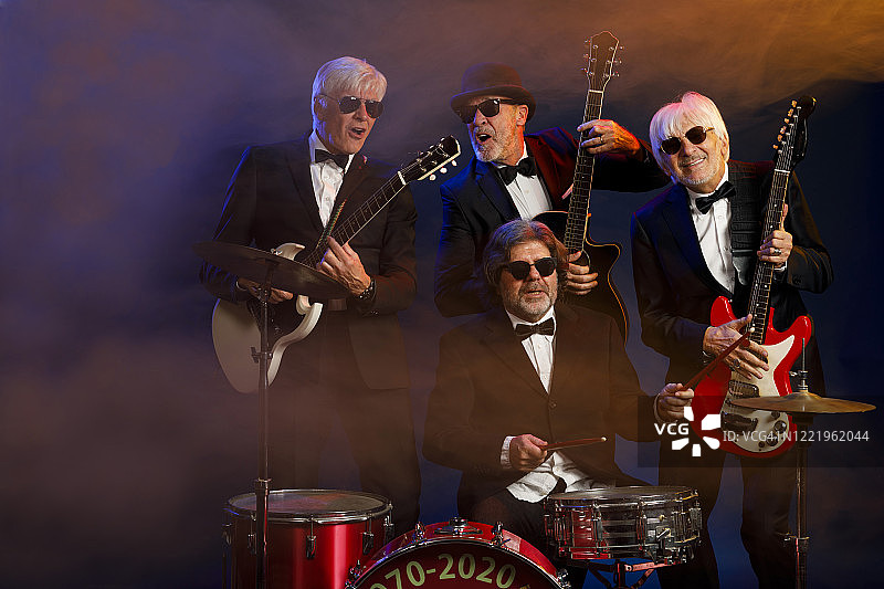 音乐家组合：吉他手和鼓手，活跃的年长男子演奏吉他和鼓。挚友。蓝色背景，有光线和烟雾特效。图片素材