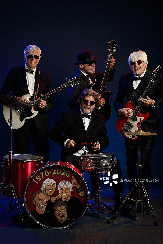 音乐家组合：吉他手和鼓手，活跃的年长男子演奏吉他和鼓。挚友。蓝色背景，有光线和烟雾特效。图片素材