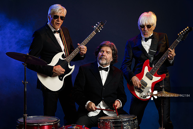 音乐家组合：吉他手和鼓手，活跃的年长男子演奏吉他和鼓。挚友。蓝色背景，有光线和烟雾特效。图片素材