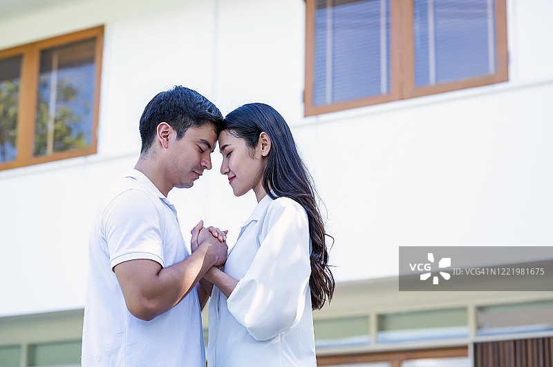 快乐的异族年轻夫妇站在他们新房子的前门前，笑着手牵着手图片素材