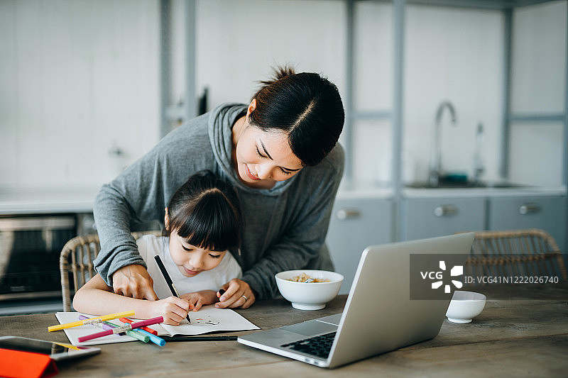 年轻的亚洲母亲在餐桌上准备健康的早餐，在家教育女儿并辅导她的功课图片素材