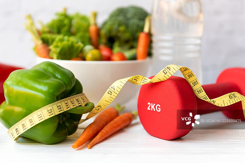 健康饮食生活方式概念：运动器械与新鲜沙拉，搭配卷尺，居家健身风格。健康生活方式概念图片素材