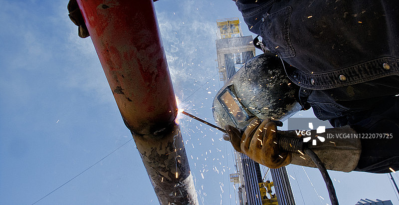 阳光明媚的日子里，油田工人在石油钻井现场焊接管道端盖图片素材