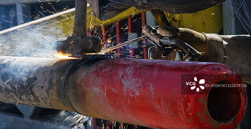 晴天，油田工人在油气钻井平台上焊接管道端盖的特写镜头，火花四溅图片素材