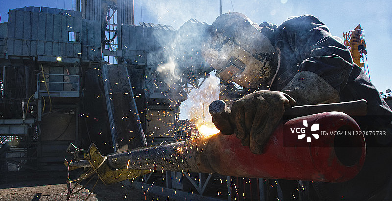 晴天，油田工人在石油和天然气钻井平台的井架旁焊接管道端盖，火花四溅图片素材