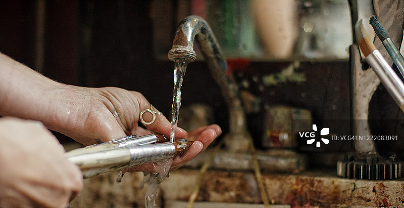 白人女艺术家在室内艺术工作室的水槽中清洗画笔图片素材