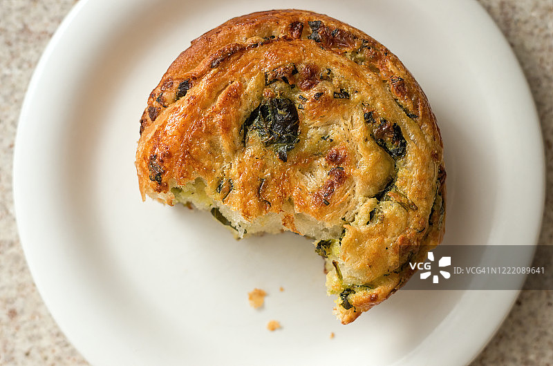 菠菜咸味酥皮卷，用类似于羊角面包的层压酵母面团制成，圆形白盘上缺少几口图片素材