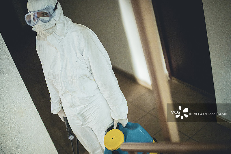 一名女子身穿防护服，对住宅楼空间进行消毒图片素材