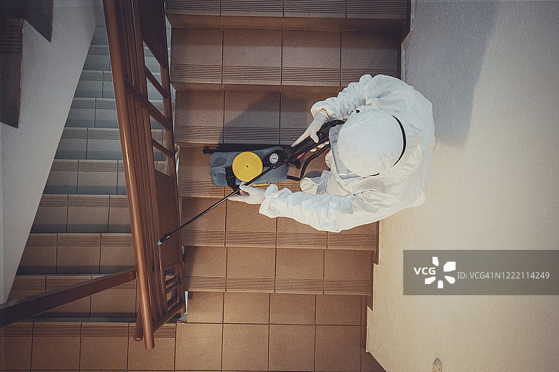 一名女子身穿防护服，对住宅楼空间进行消毒图片素材