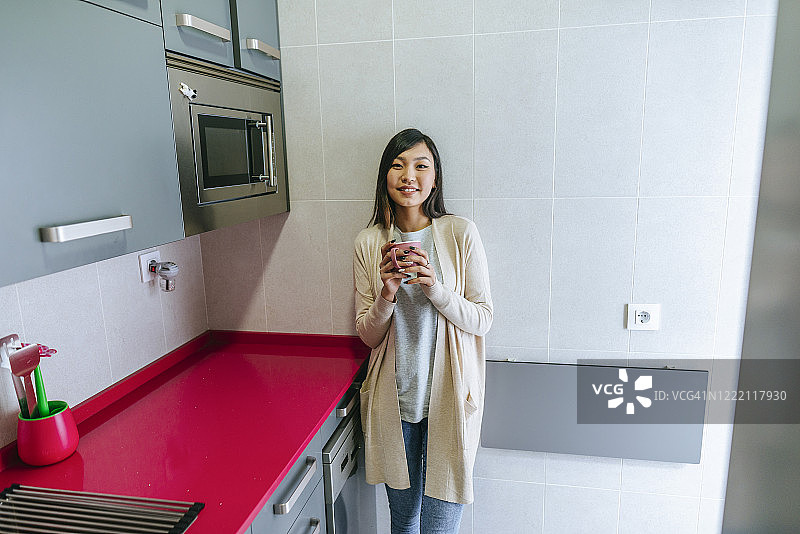 在厨房里拿着杯子看着镜头的休闲女人图片素材