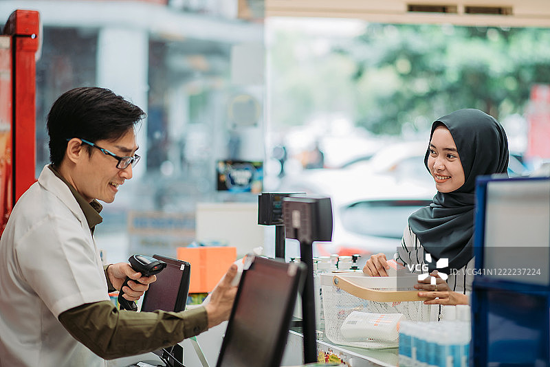亚洲马来微笑顾客看着药剂师在药房收银台扫描产品图片素材
