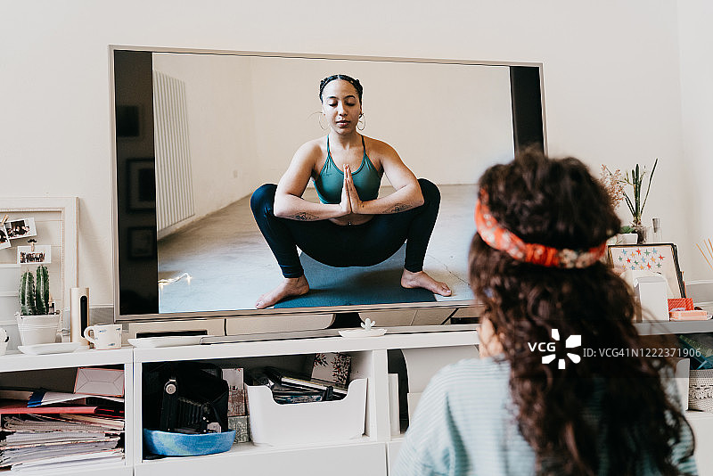女人在家通过电视上的视频课程练习瑜伽图片素材
