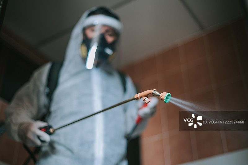 一位亚洲华裔男子身穿防护服喷洒房屋，对公寓进行消毒，进行虫害控制图片素材