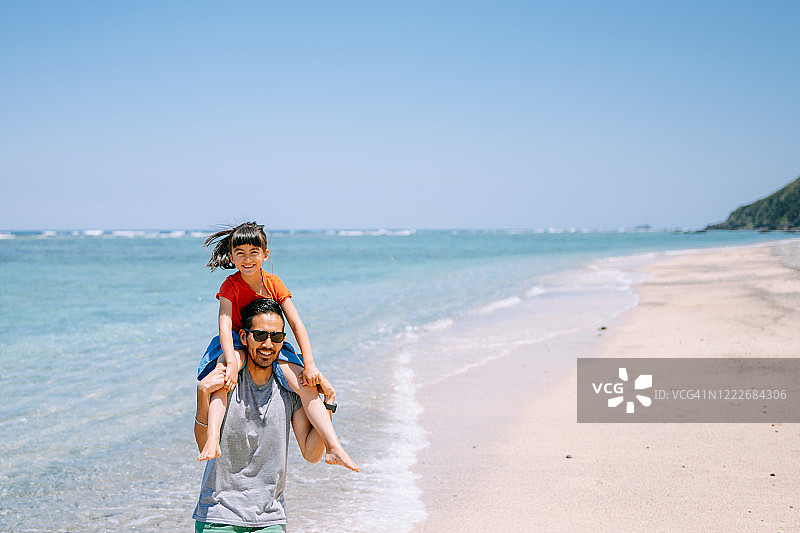 父亲扛着小女孩在热带海滩上奔跑图片素材