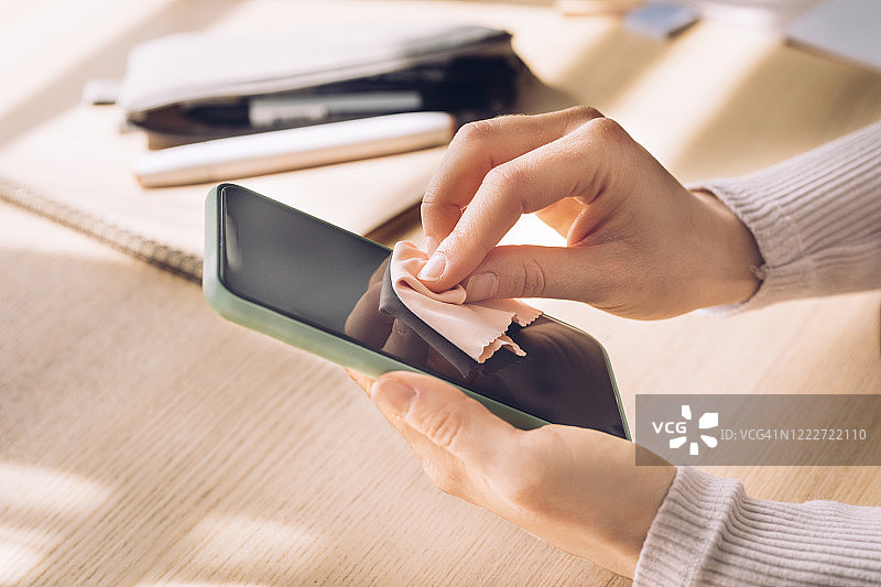 设备消毒预防病毒：匿名女性擦拭手机屏幕图片素材
