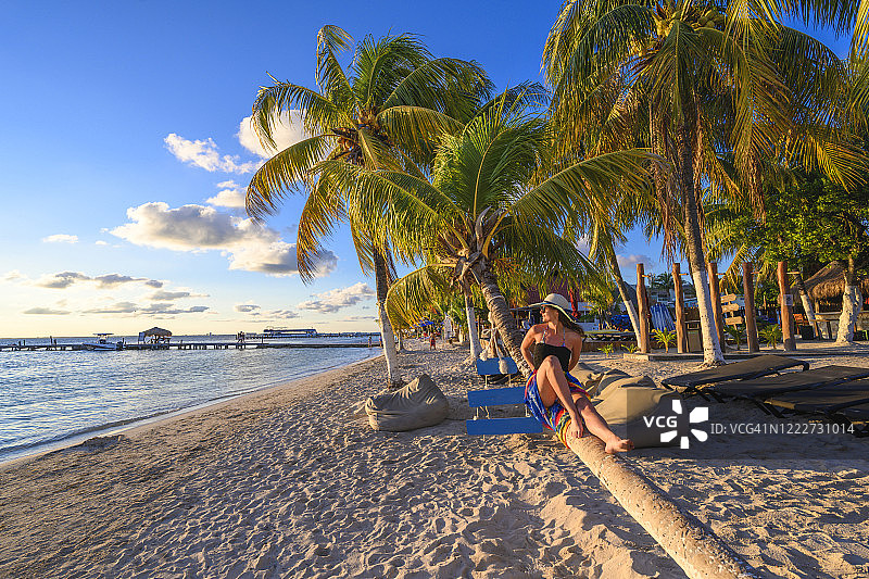 在墨西哥加勒比海滩日落时躺在棕榈树上的女人图片素材