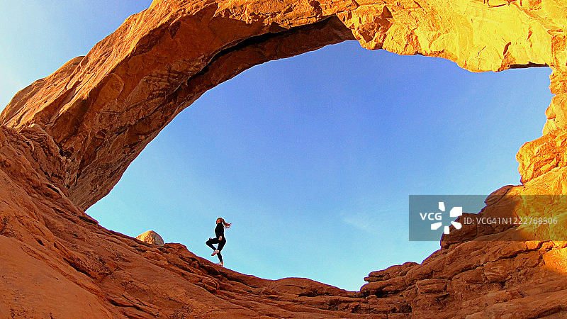 女人在美国拱门国家公园的天然拱门下跑步图片素材