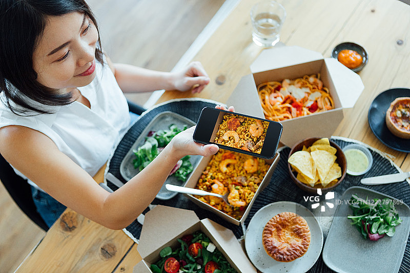 年轻女子在家吃外卖时用智能手机拍照图片素材