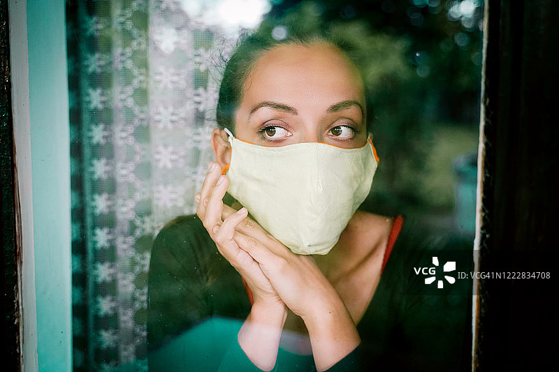 隔离期间戴着口罩看窗外的年轻女人图片素材