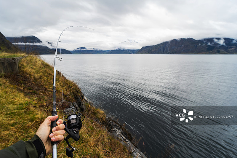 在挪威峡湾海边用鱼竿钓鱼的视角图片素材