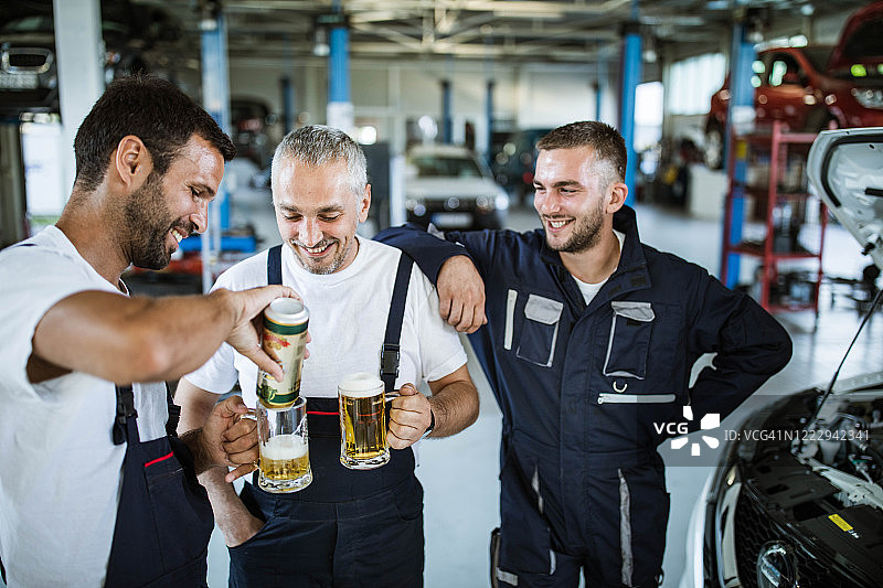 快乐的汽车修理工在车间休息时喝啤酒图片素材
