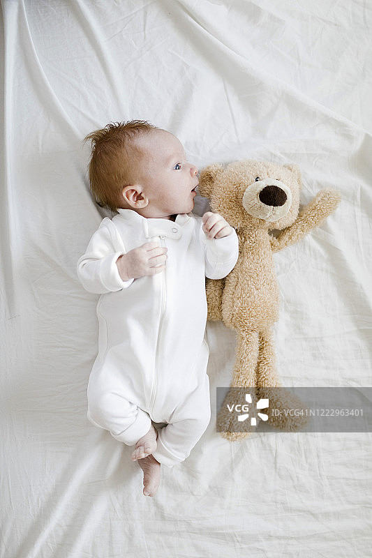 和泰迪熊一起躺在床上的男婴（2-5个月）图片素材