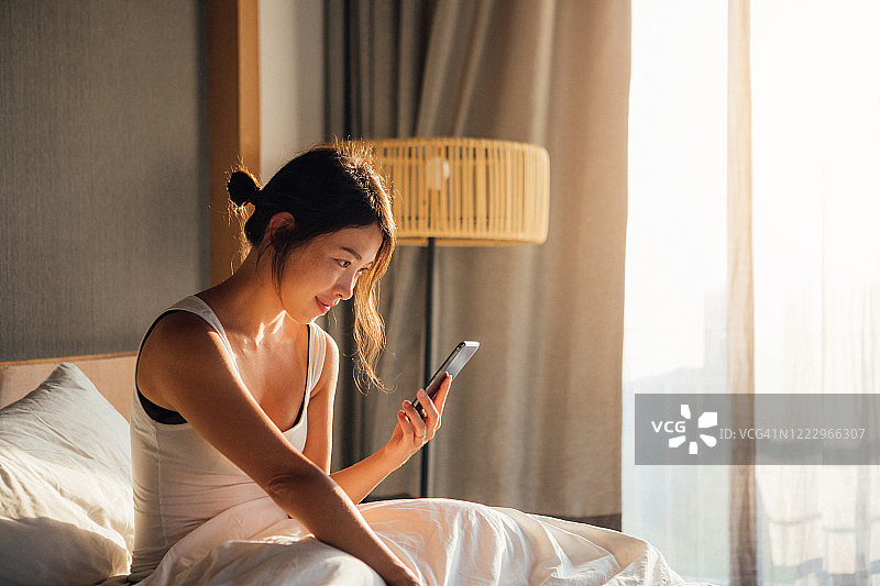 年轻女人在床上醒来时使用智能手机图片素材