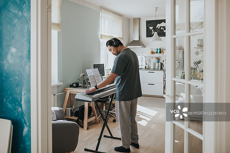 亚洲男人在封锁期间在家练习电子琴图片素材