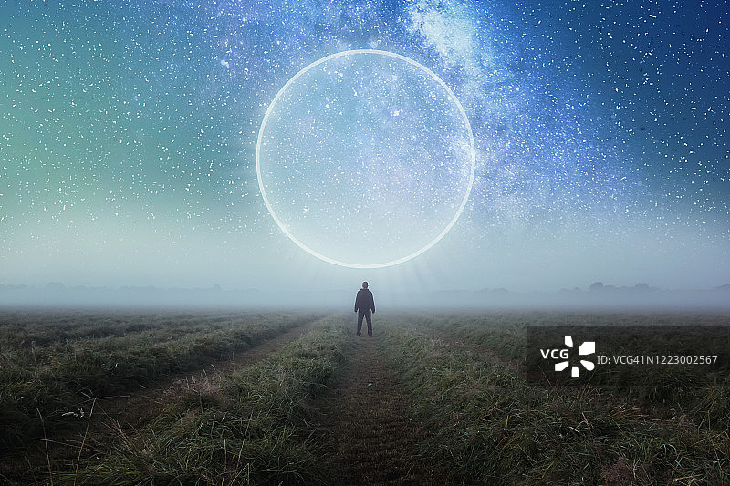科幻概念：男子站在田野里，眺望夜空中发光的传送门图片素材