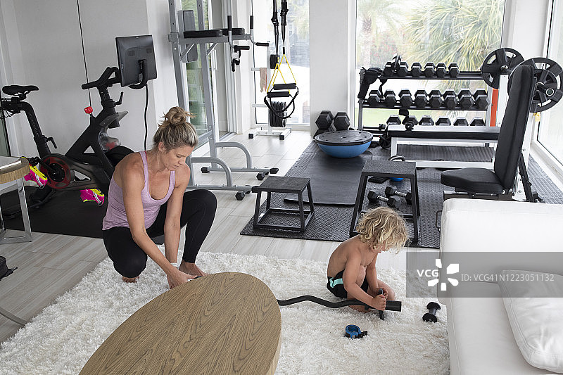 母亲在家用健身房帮助幼儿儿子在杠铃上增加重量图片素材