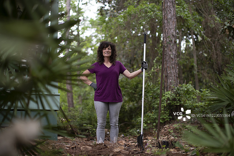 在院子里自豪地拿着耙子的中年妇女图片素材