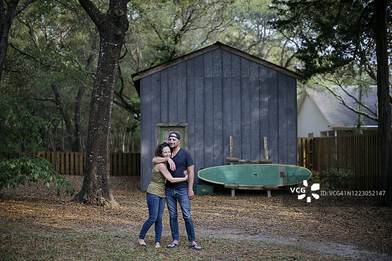 在佛罗里达州，夫妻在后院小屋和冲浪板前拥抱图片素材