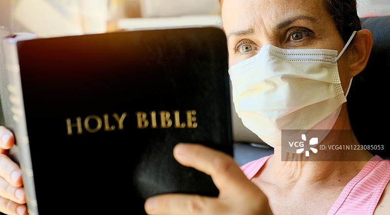 戴着外科口罩阅读圣经的中年妇女图片素材