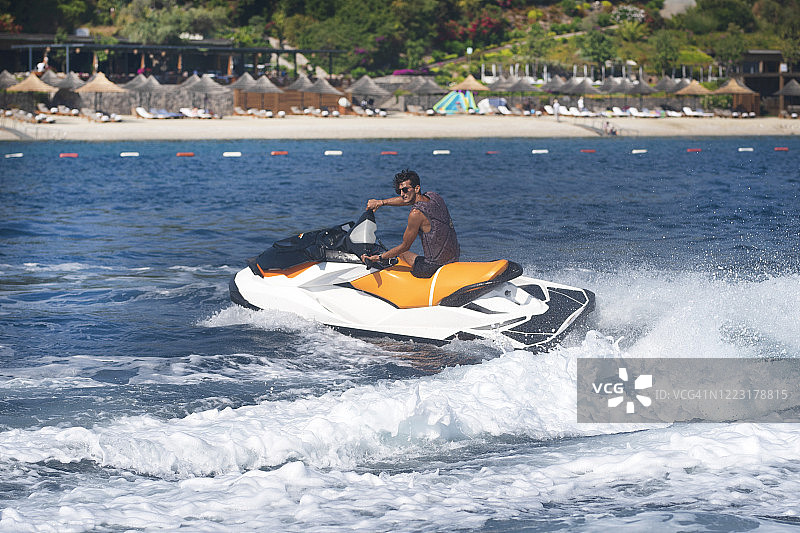 晴朗的一天，男人驾驶着橙色水上摩托艇在碧绿的海面上行驶图片素材