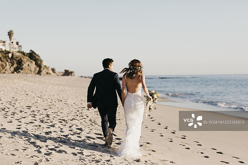 幸福的新娘夫妇在海滩上奔跑的背影图片素材