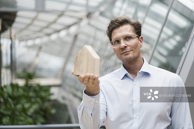 建筑师手持木制房屋模型，站在可持续建筑前图片素材