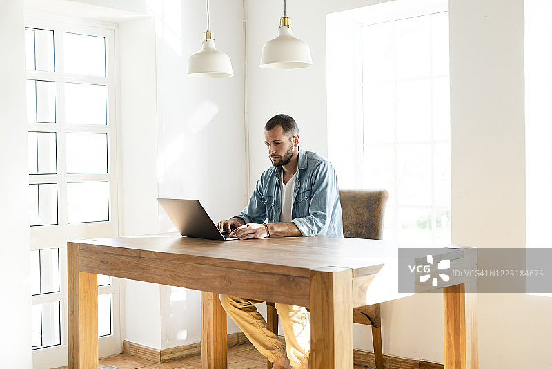 在现代客厅的家庭办公室里用笔记本电脑工作的年轻男人图片素材