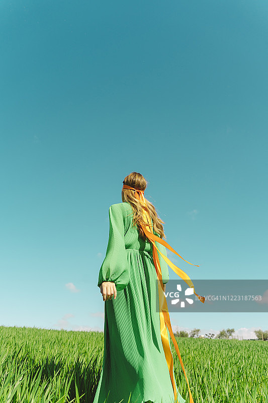 戴着丝带，站在田野里，身穿绿色连衣裙的年轻女子背影图片素材