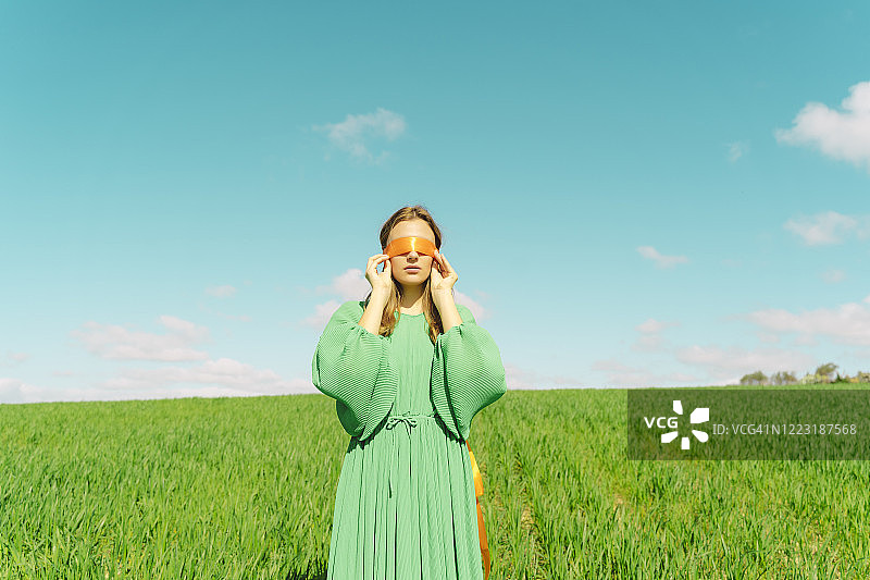 蒙着眼睛，穿着绿色连衣裙站在田野里的年轻女人图片素材