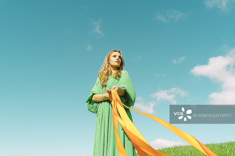 在田野里手持彩带的绿裙年轻女子图片素材