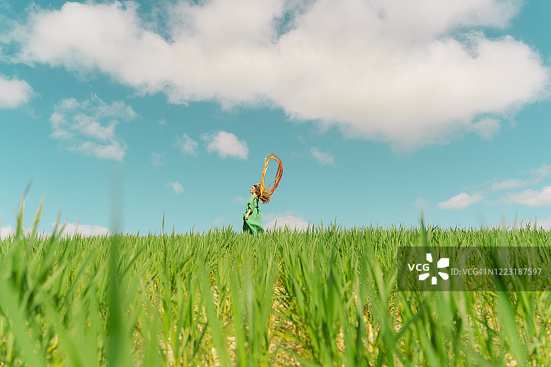 年轻女人身穿绿色连衣裙，站在田野里，彩带飘扬图片素材