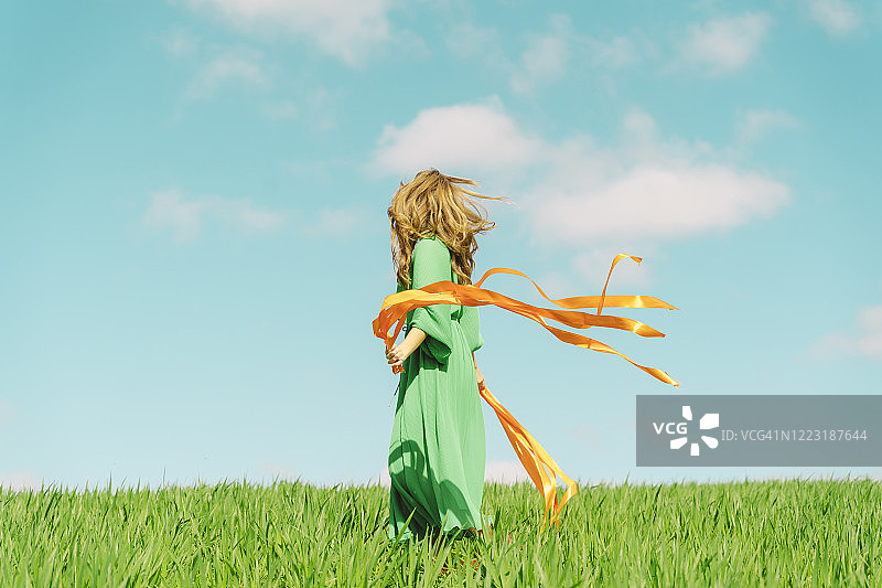 年轻女人身穿绿色连衣裙，站在田野里，彩带飘扬图片素材