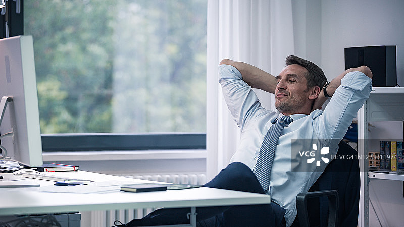 坐在办公室桌前，自信地沉思的白领商人图片素材