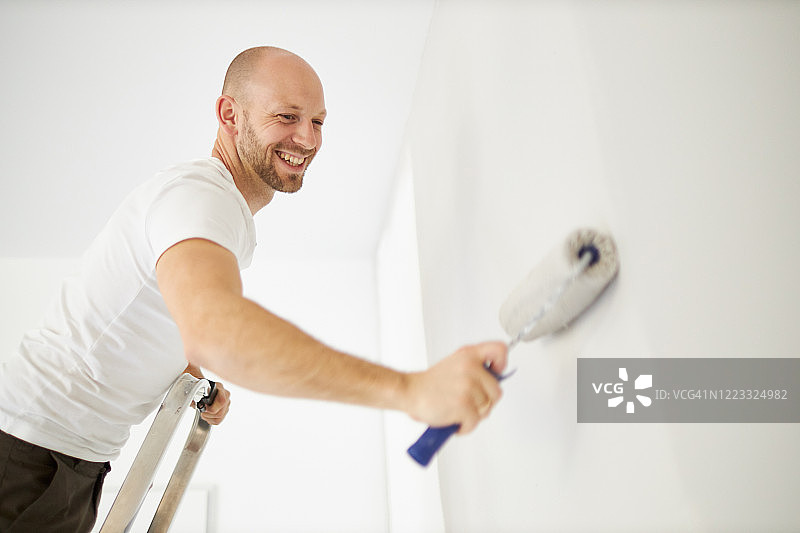 中年男人用滚筒刷在自家墙上刷漆图片素材