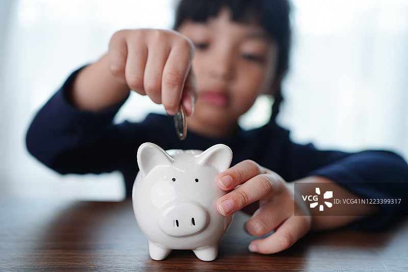 亚洲小女孩往存钱罐放硬币图片素材