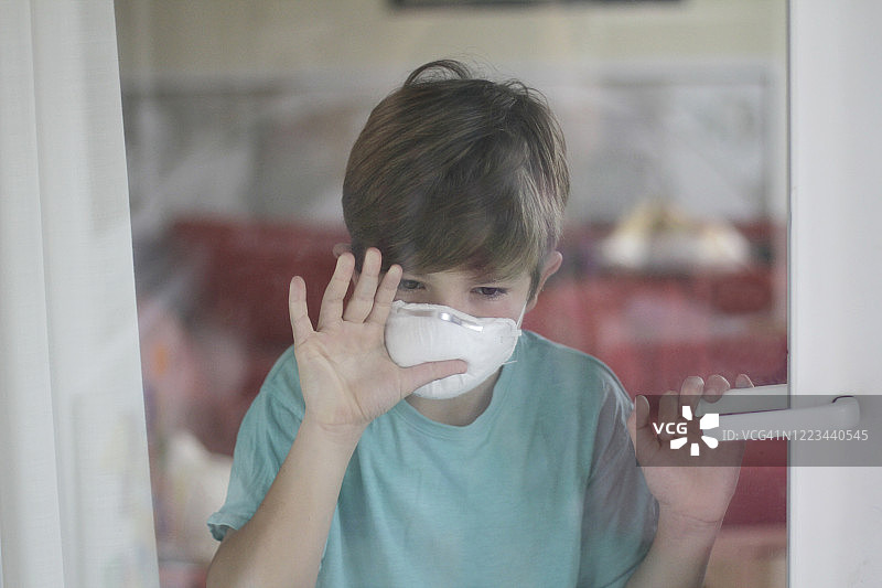 新冠疫情居家隔离期间，戴口罩向外看的男孩图片素材