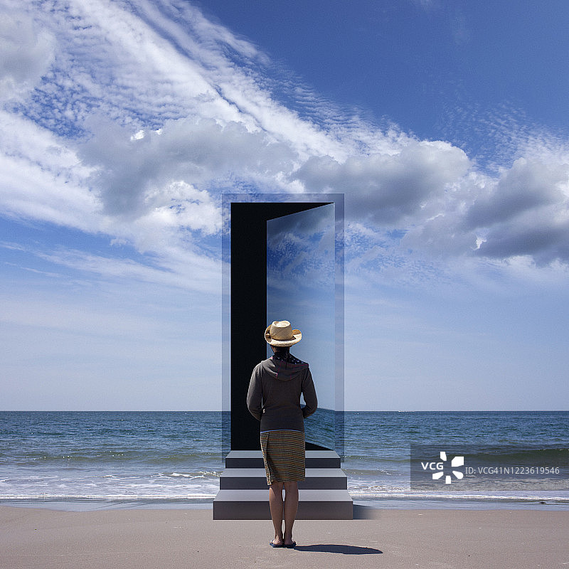 年轻女子在海滩上面对风景中的一扇打开的门图片素材
