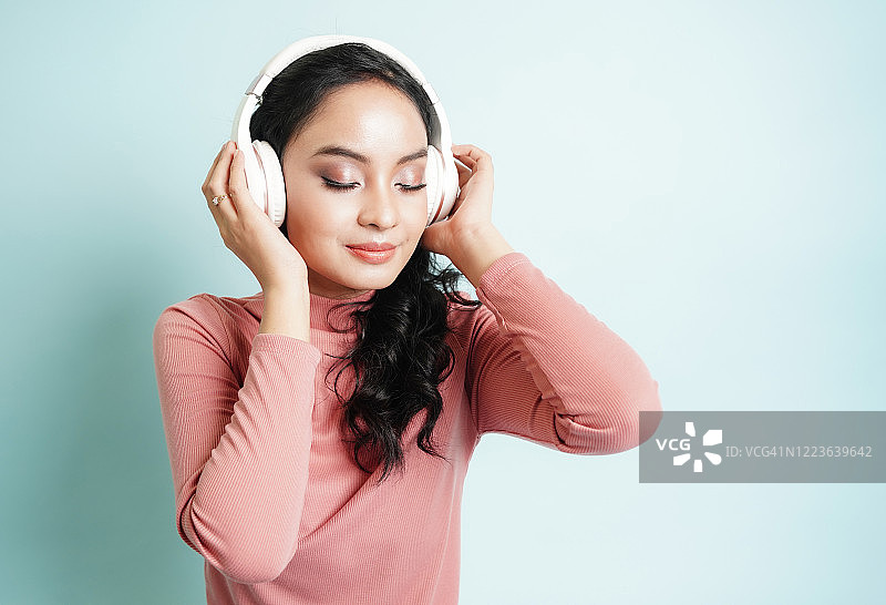 快乐的亚洲少女用无线耳机听MP3播放器里的歌，放松和音乐爱好者概念图片素材