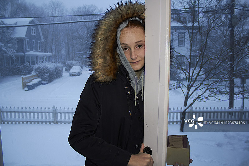 站在家门口向内看的少女，外面是白雪皑皑的街区图片素材
