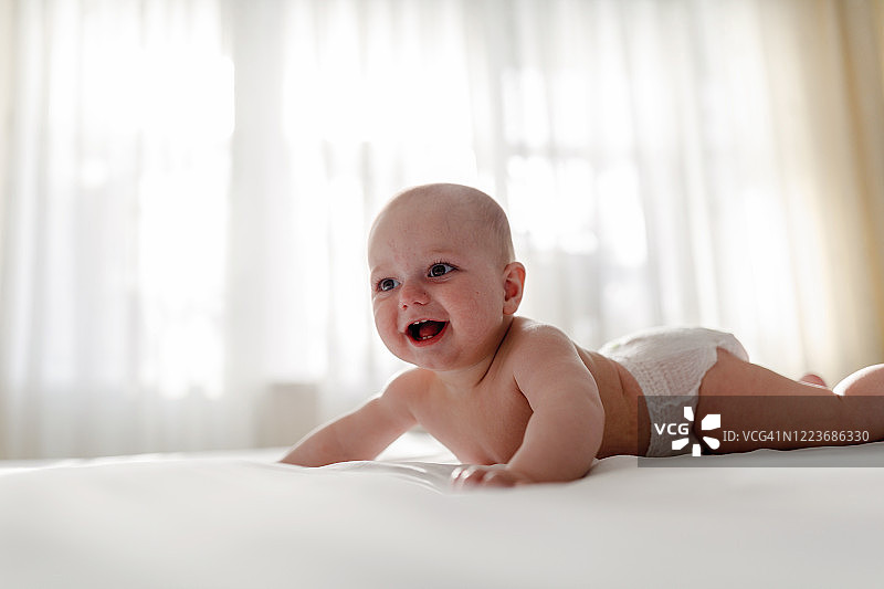 可爱的光脚孩子穿着尿布，在白色床上用品上玩耍时微笑图片素材